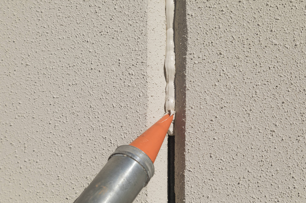 Caulking gun applying sealant in an expansion joint on stucco wall