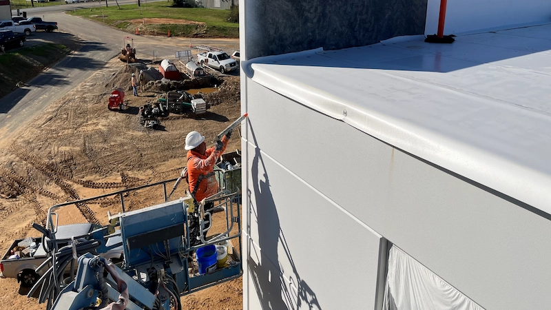 A picture of a man on a lift using a sealant on a commercial building.